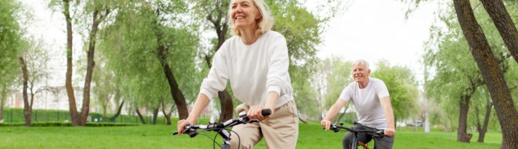 An elderly couple riding their bikes in the park.